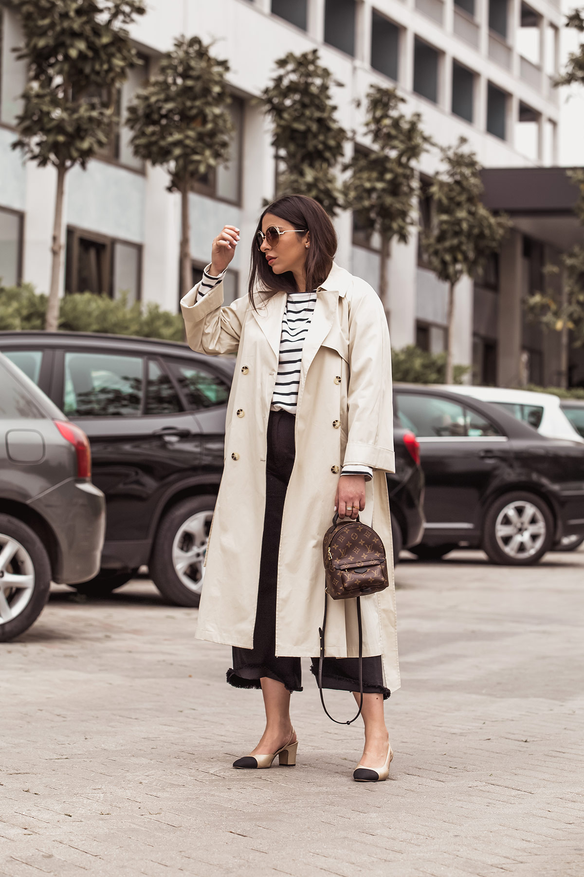 Stella Asteria wearing classic look with beige trench coat, breton top, Louis Vuitton Palm Springs backpack as a cross body, black denim culottes, Chanel slingbacks and Chloe Carlina sunglasses