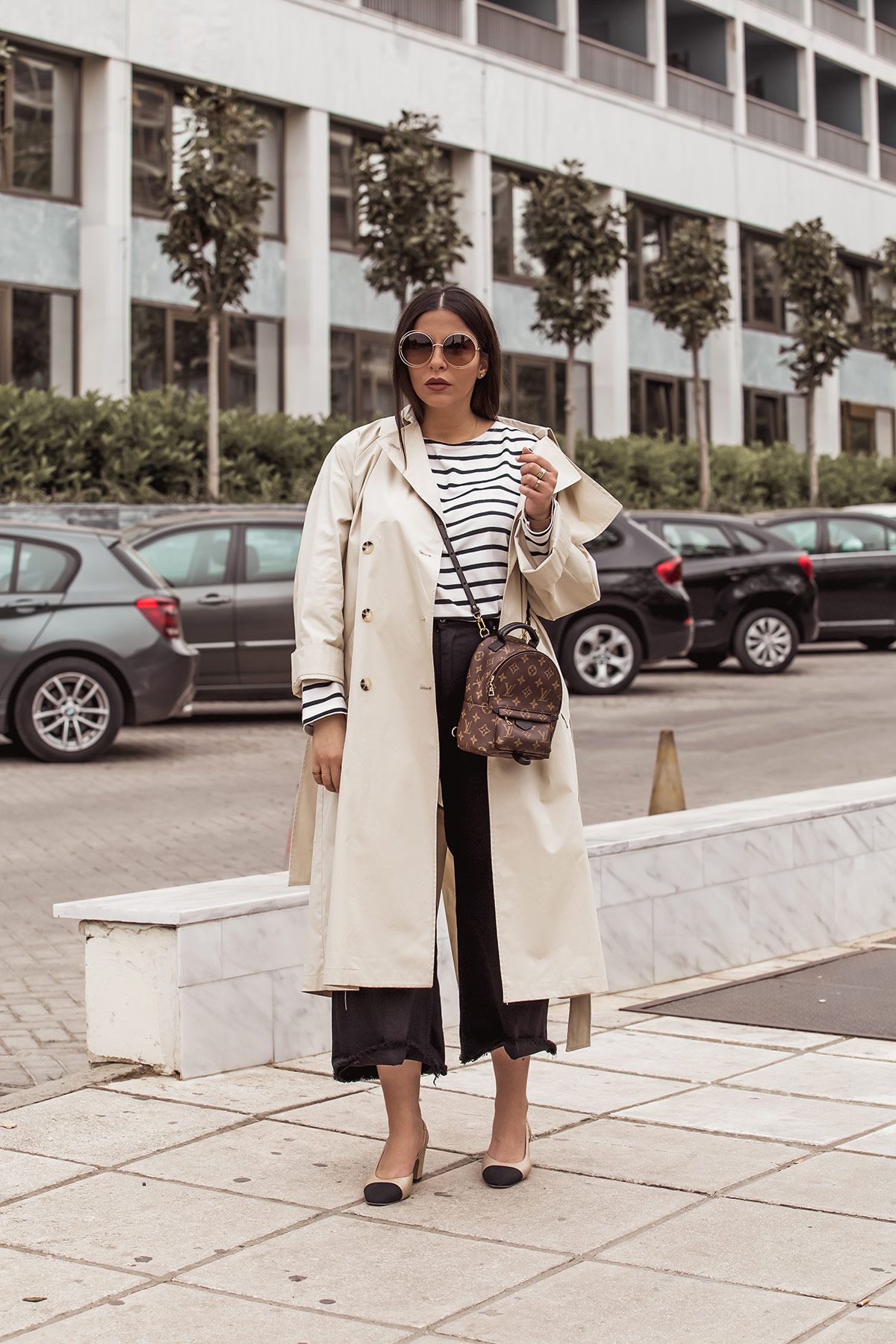Stella Asteria wearing classic look with beige trench coat, breton top, Louis Vuitton Palm Springs backpack as a cross body, black denim culottes, Chanel slingbacks and Chloe Carlina sunglasses