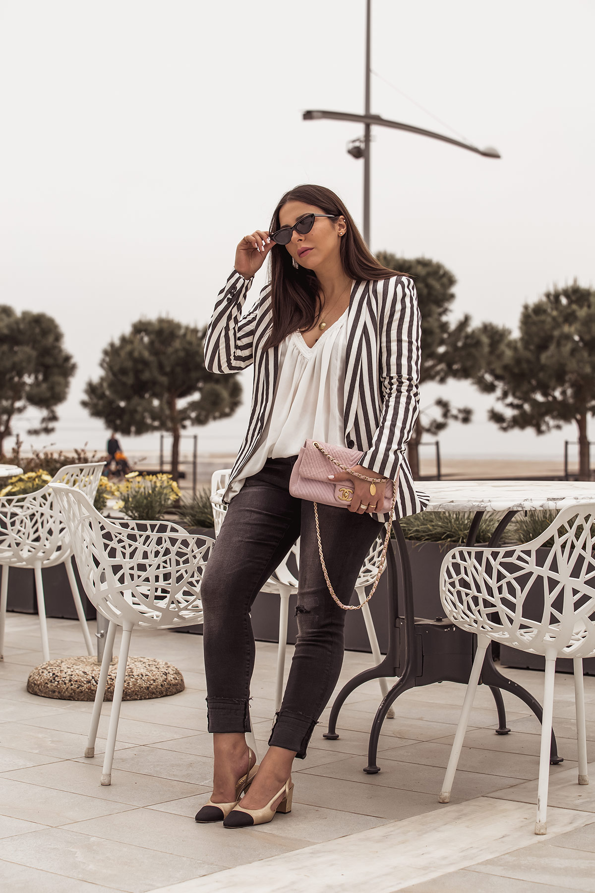 Stella Asteria showing how to wear a striped blazer for spring - striped blazer from H&M, dark grey jeans, Chanel slingbacks, white top and pink Chanel chevron bag, Le Specs cat-eye sunglasses